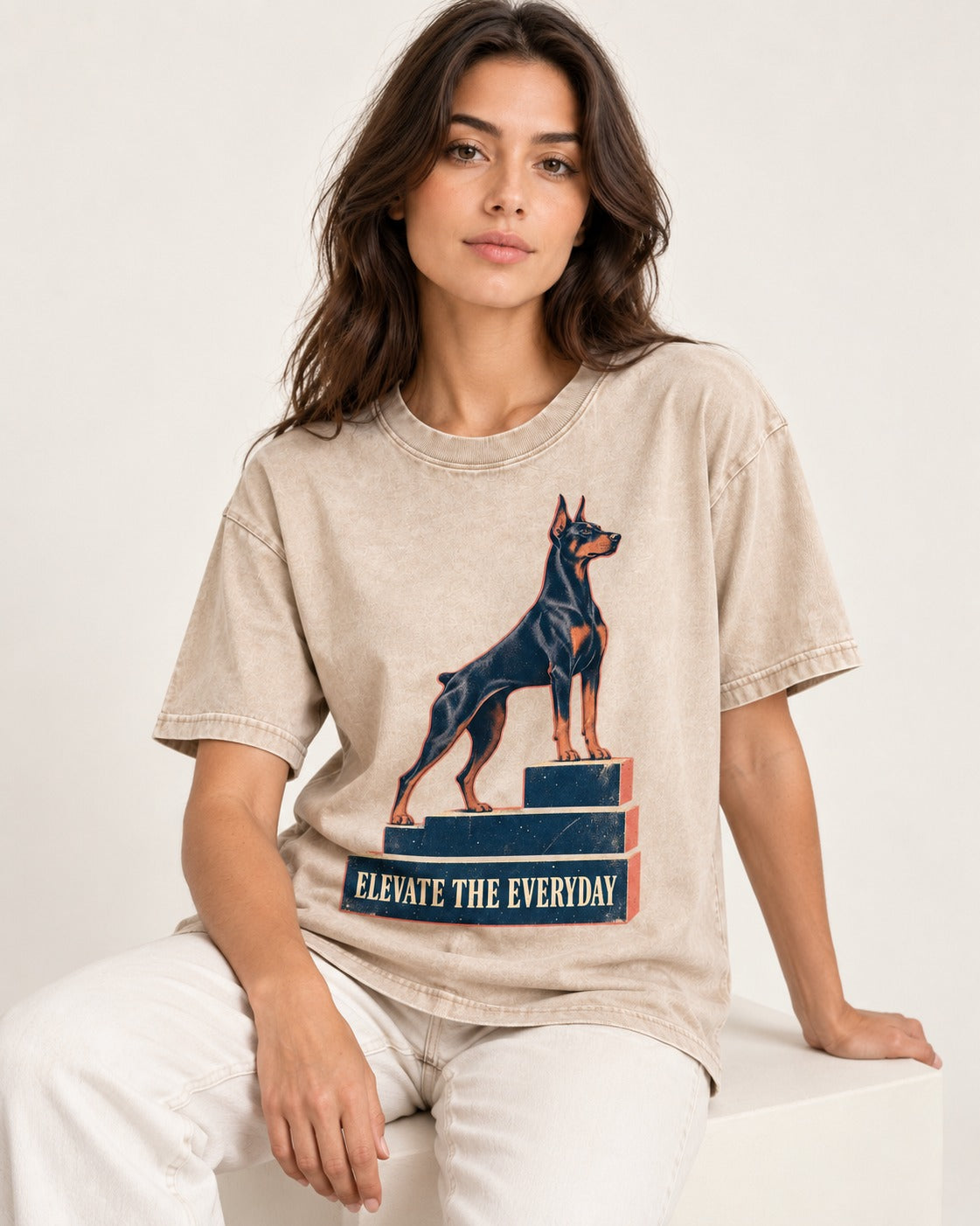 Doberman Elevate the Everyday Podium Graphic Washed Tee in Apricot, worn by a seated model