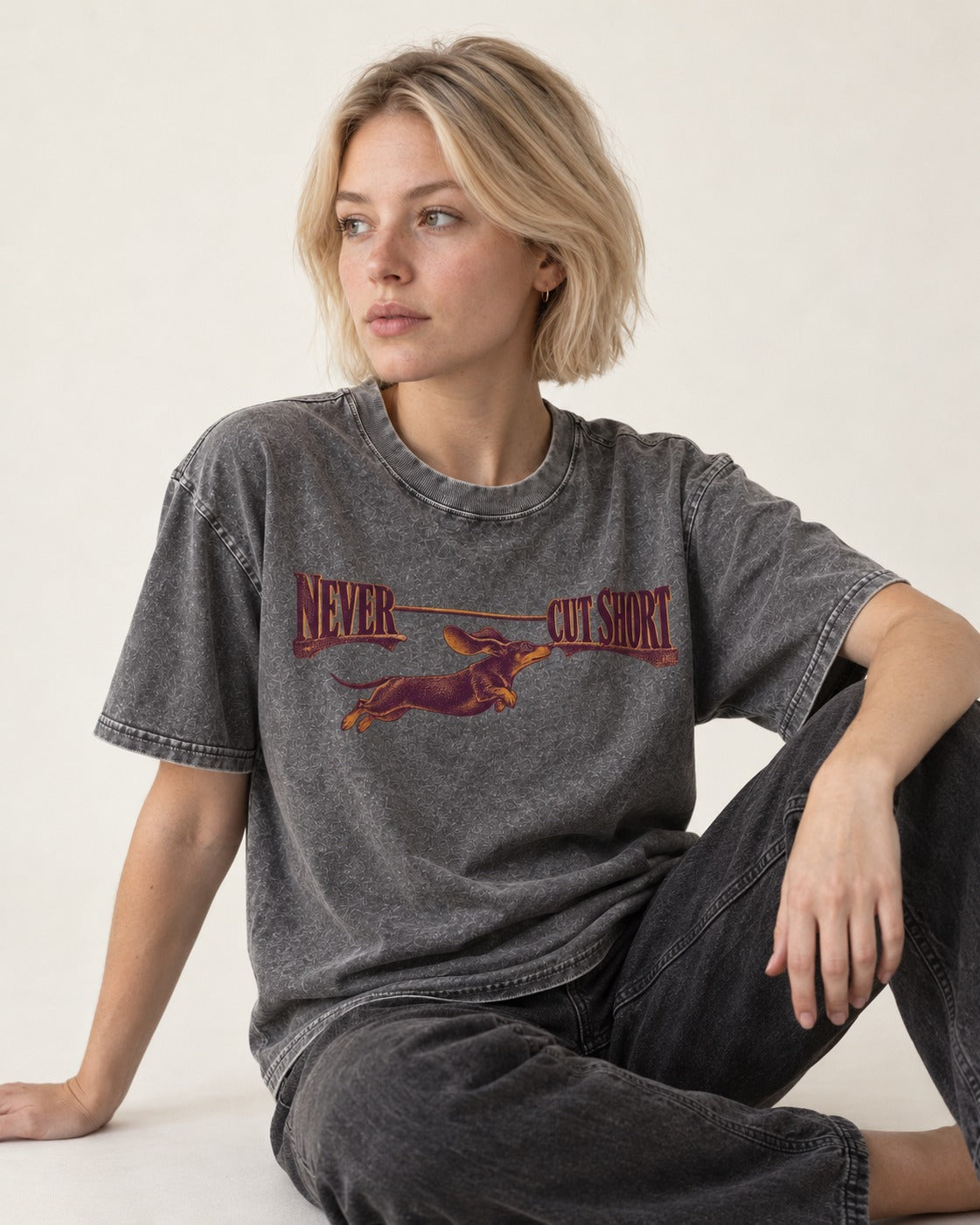 Dachshund Never Cut Short Leaping Wordmark Graphic Washed Tee in Gray, worn by a seated model