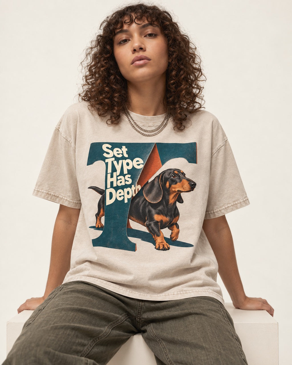 Dachshund Set Type Has Depth Folded Letter Graphic Washed Tee in Apricot, worn by a seated model