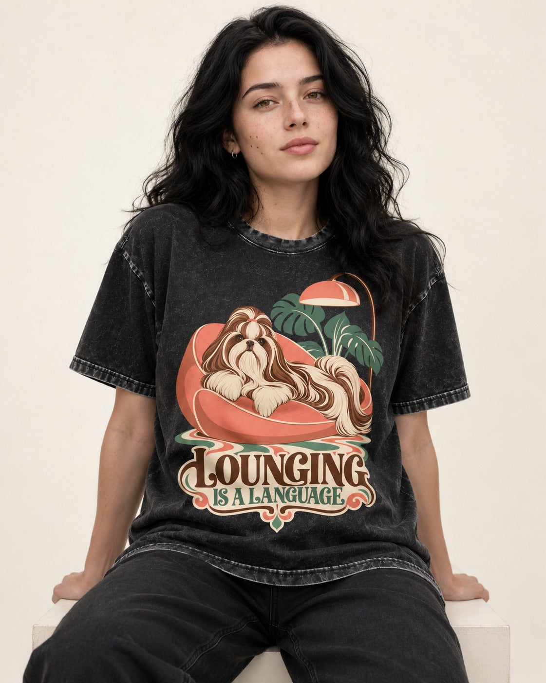 Shih Tzu Lounging Is a Language Retro Lounge Graphic Washed Tee in Black, worn by a seated model