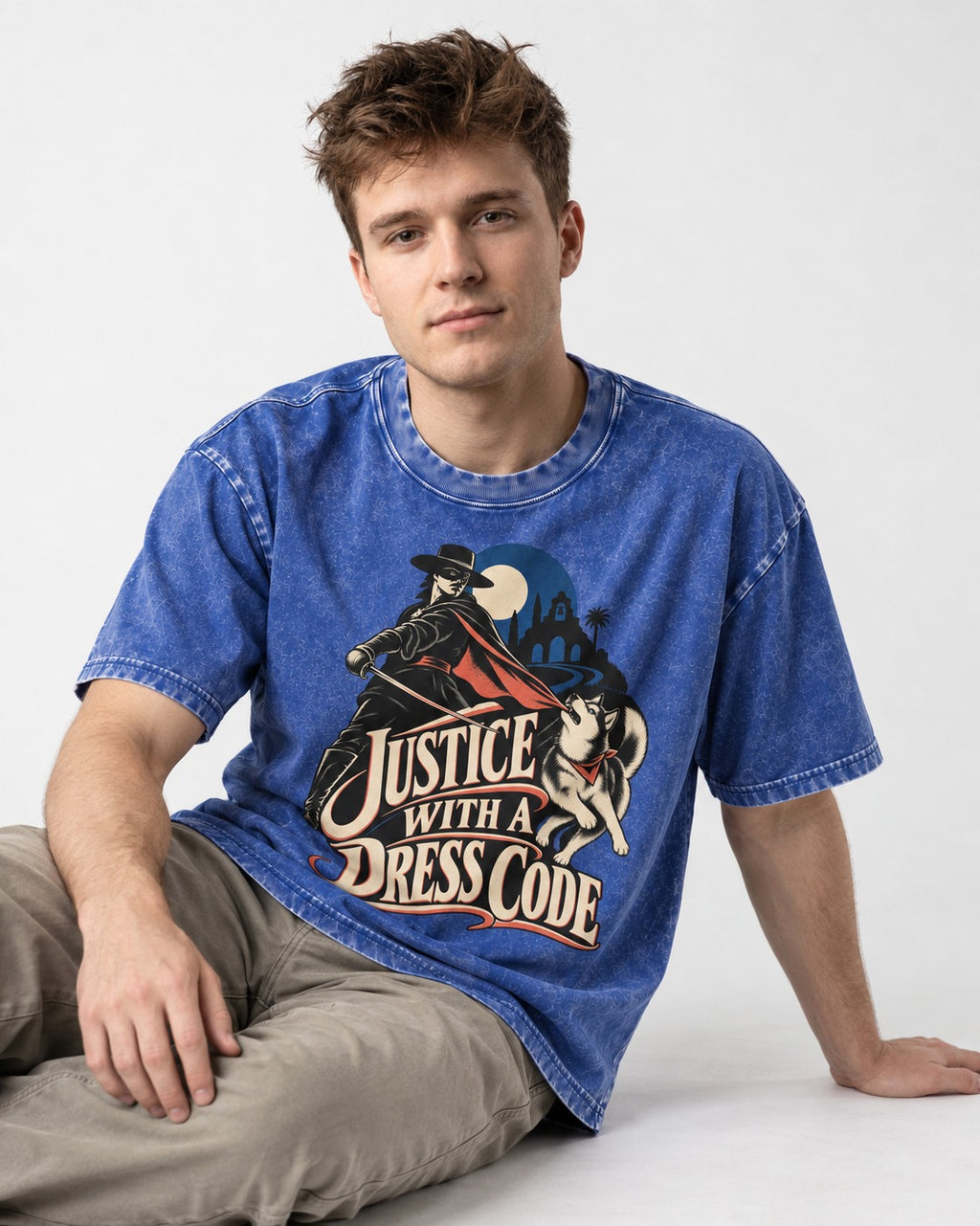 Husky Justice With A Dress Code Masked Swordsman Graphic Washed Tee in Royal Blue, worn by a seated model