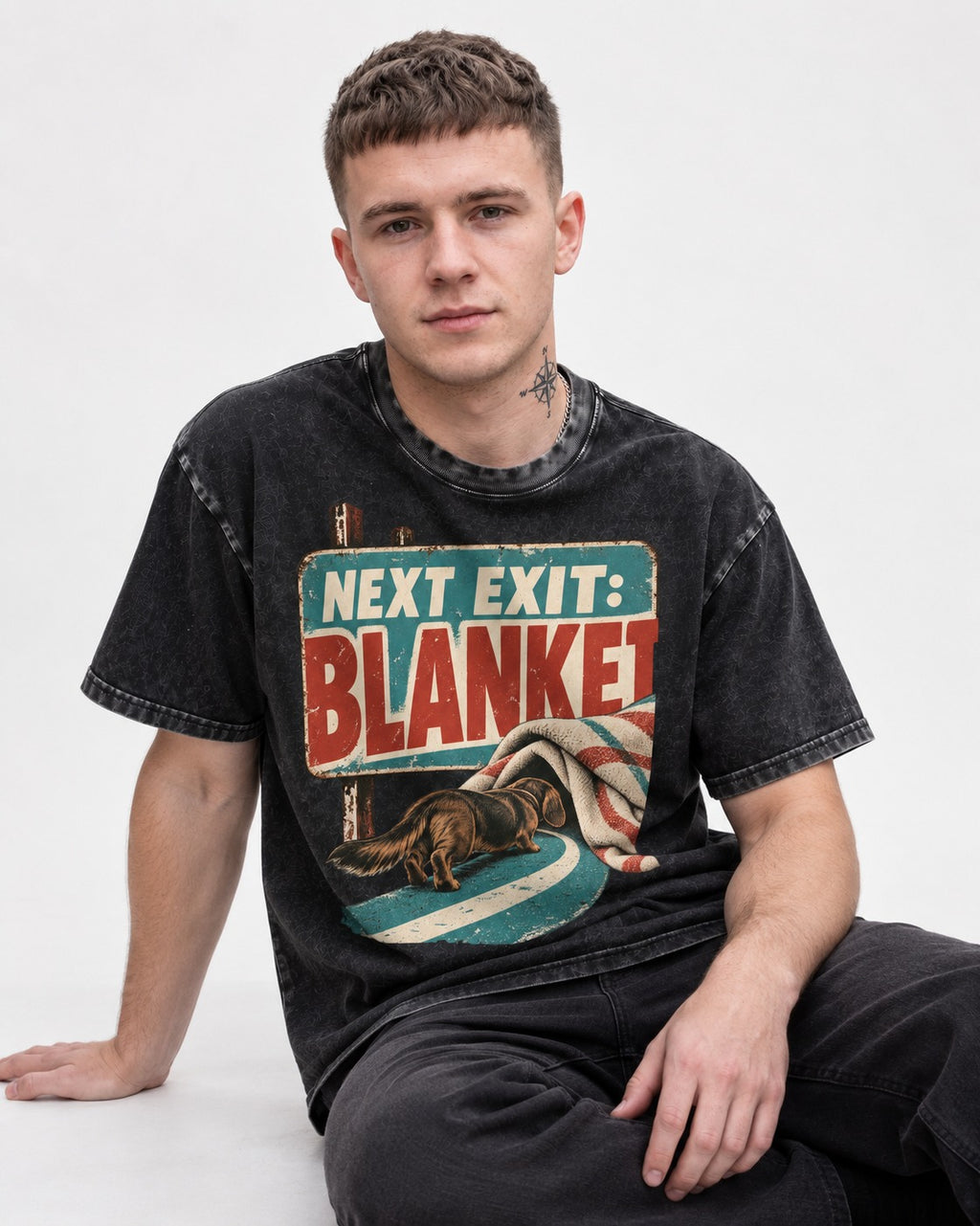 Dachshund Next Exit Blanket Road Sign Graphic Washed Tee in Black, worn by a seated model