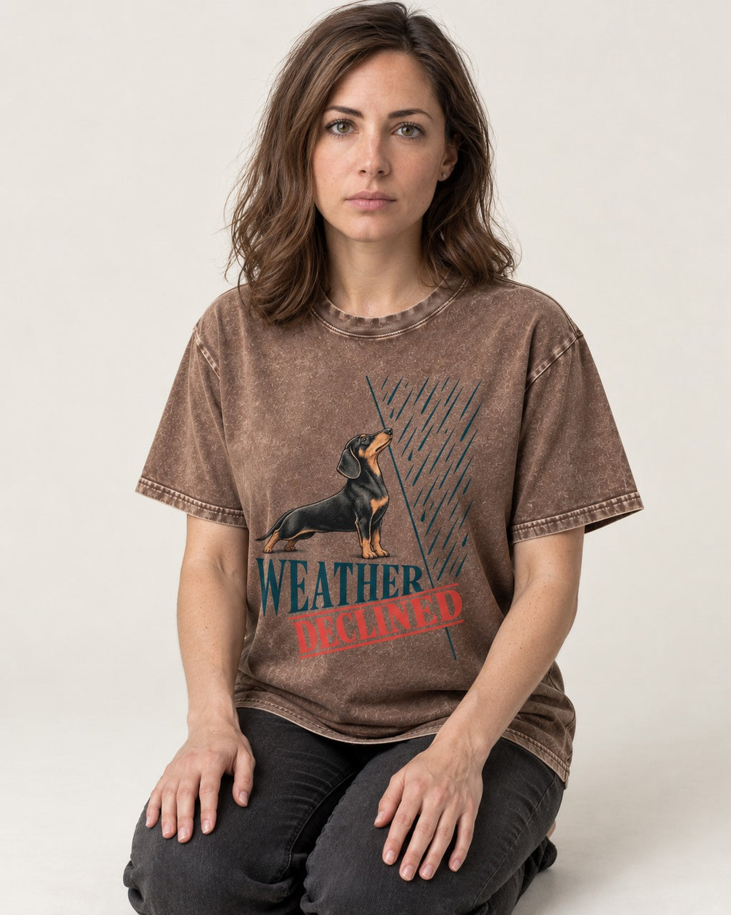 Weather Declined by Dachshund Washed Tee in Coffee, worn by a seated model