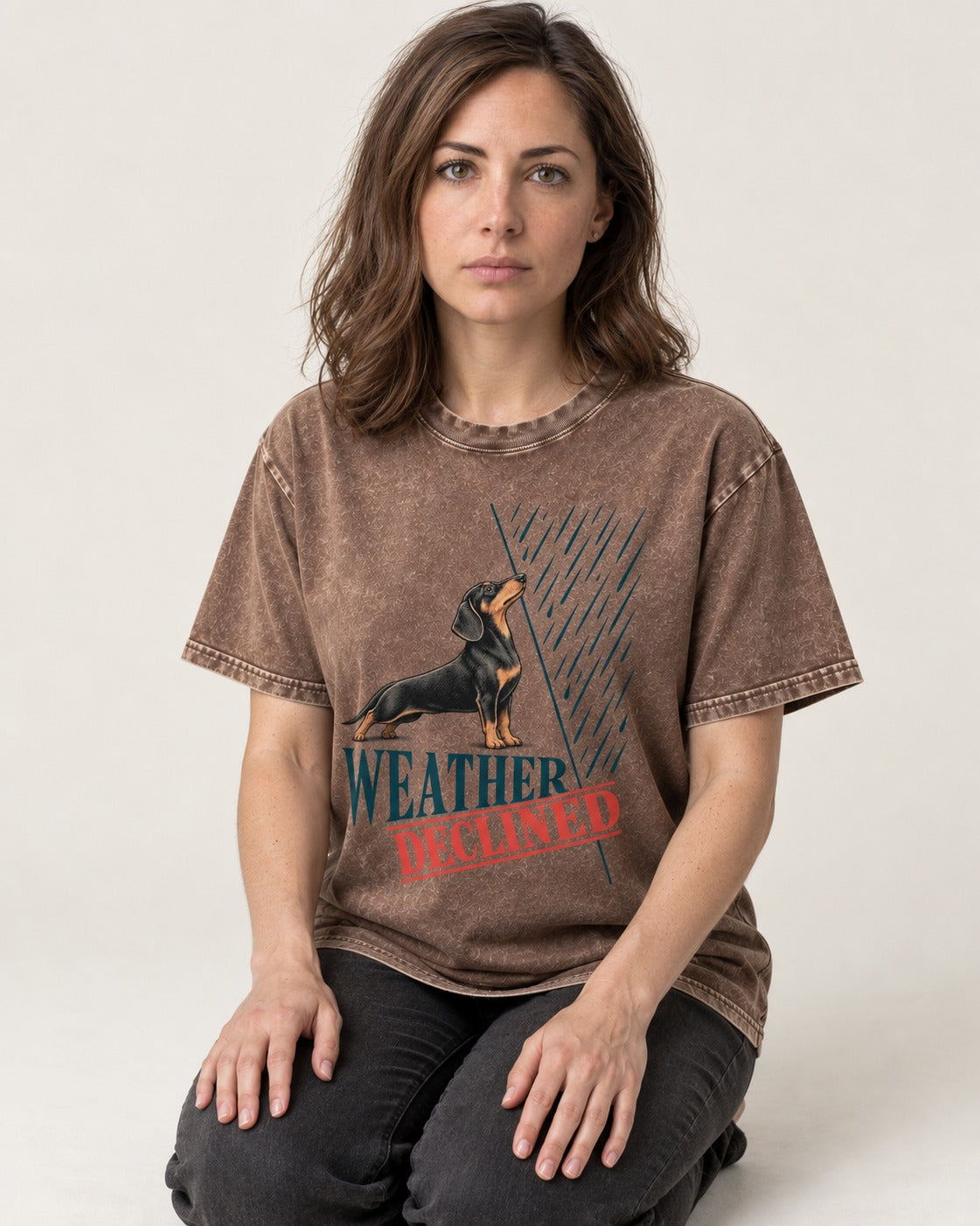 Weather Declined by Dachshund Washed Tee in Coffee, worn by a seated model