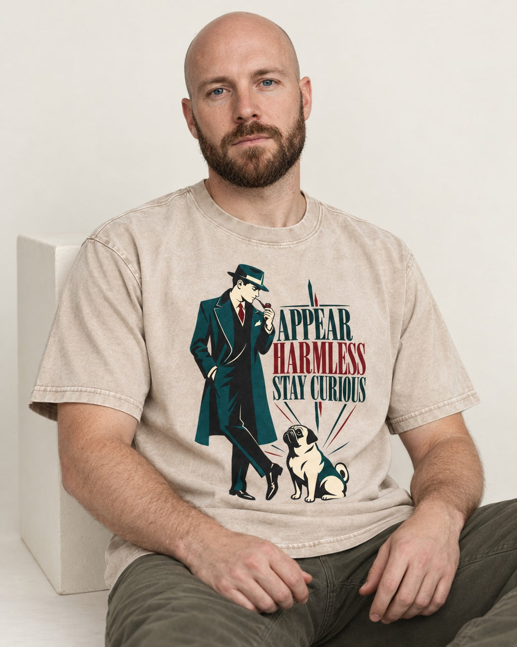 Pug Appear Harmless Stay Curious Washed Tee in Apricot, worn by a seated model