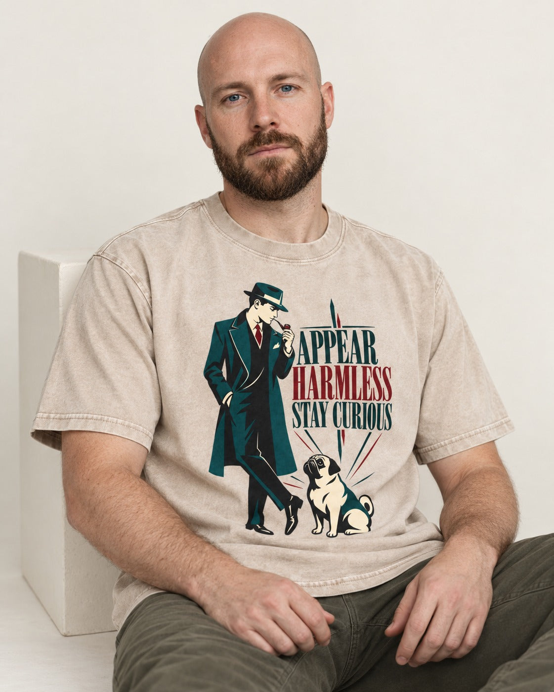 Pug Appear Harmless Stay Curious Washed Tee in Apricot, worn by a seated model