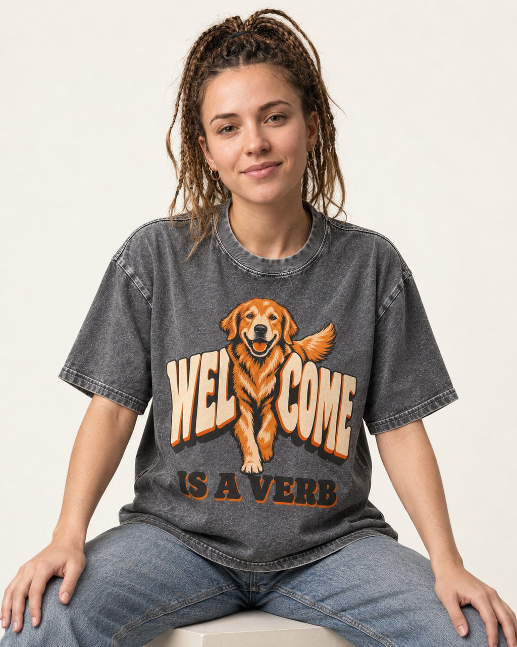 Golden Retriever Welcome Is a Verb Washed Tee in Gray, worn by a seated model