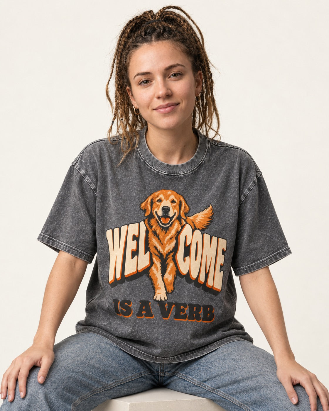 Golden Retriever Welcome Is a Verb Washed Tee in Gray, worn by a seated model