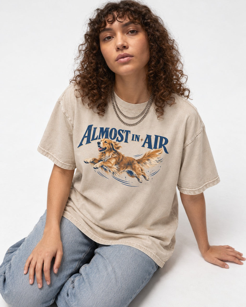 Golden Retriever Almost in Air Flying Graphic Washed Tee in Apricot, worn by a seated model