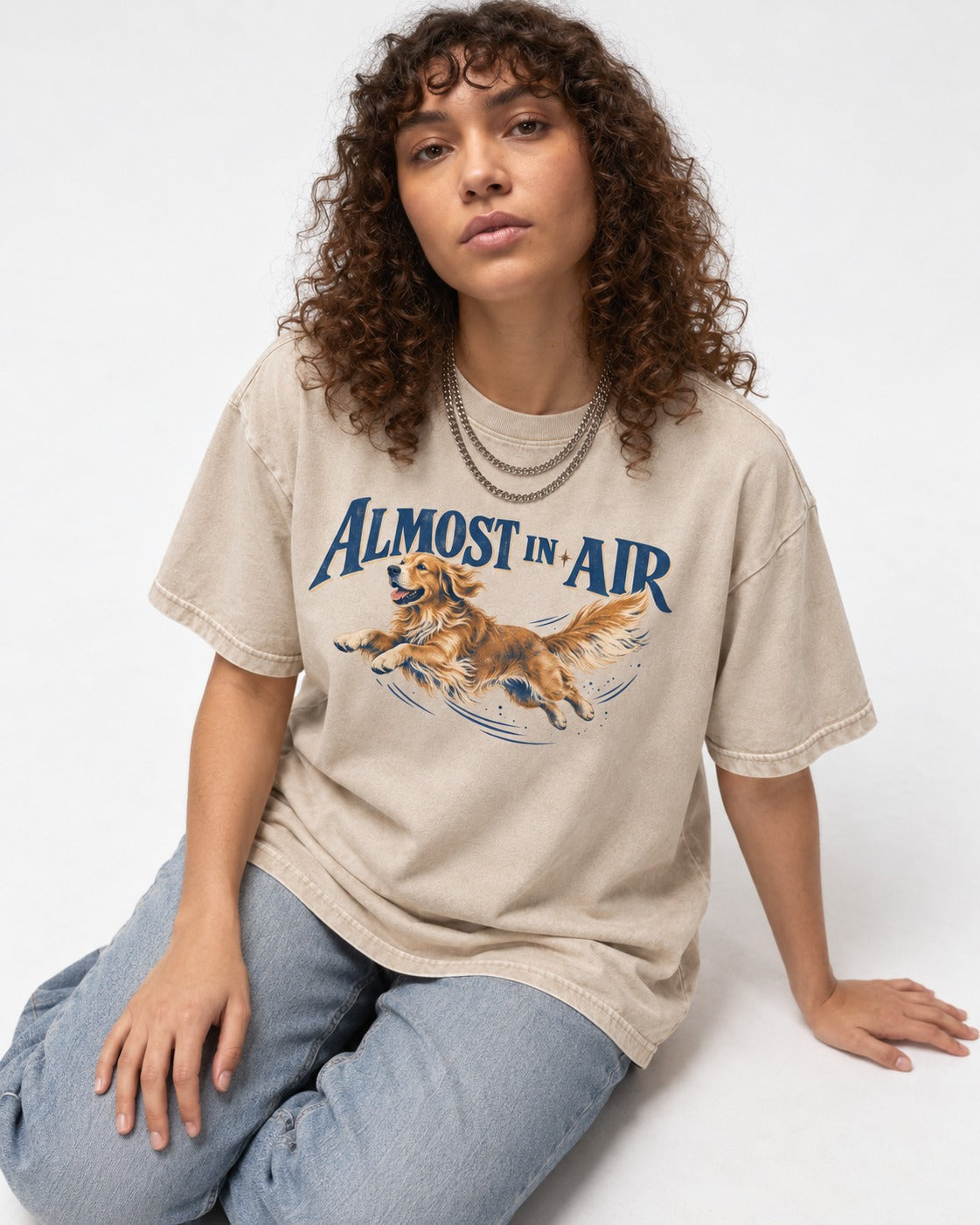 Golden Retriever Almost in Air Flying Graphic Washed Tee in Apricot, worn by a seated model