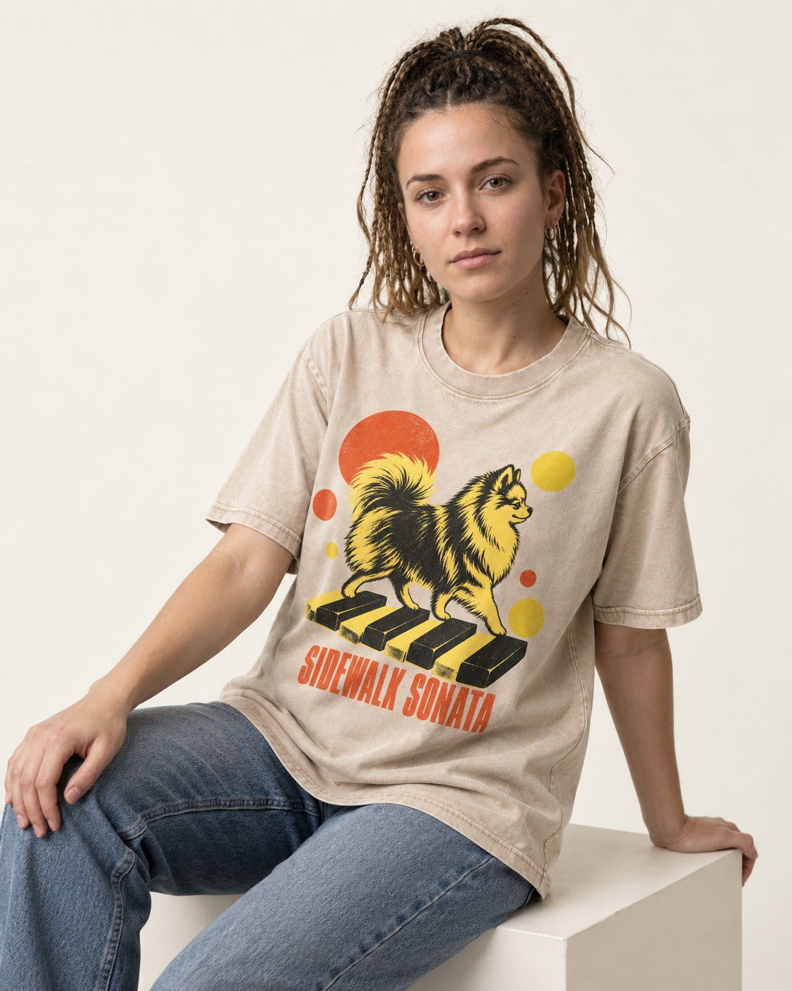 Pomeranian Sidewalk Sonata Piano Graphic Washed Tee in Apricot, worn by a seated model