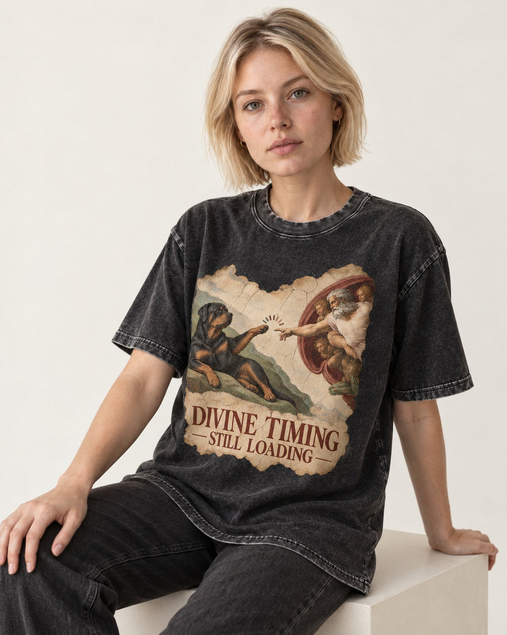 Rottweiler Divine Timing Still Loading Creation Parody Graphic Washed Tee in Black, worn by a seated model