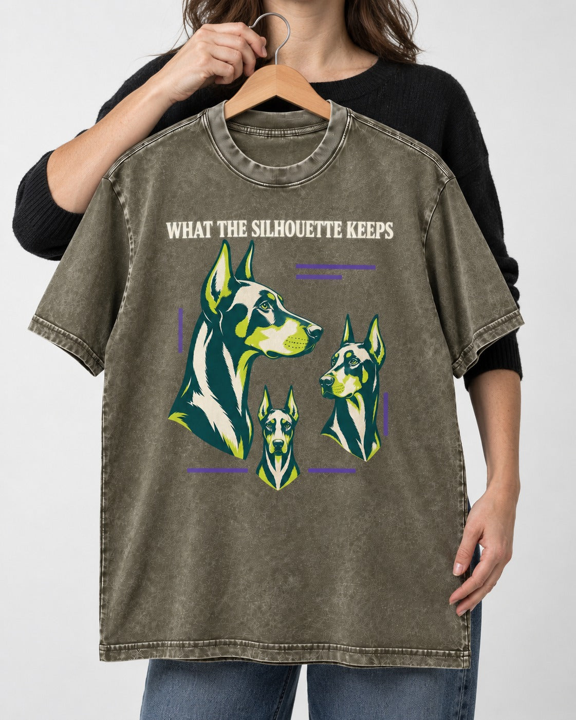 Doberman What the Silhouette Keeps Three Portrait Graphic Washed Tee in Army Green, held up on a hanger