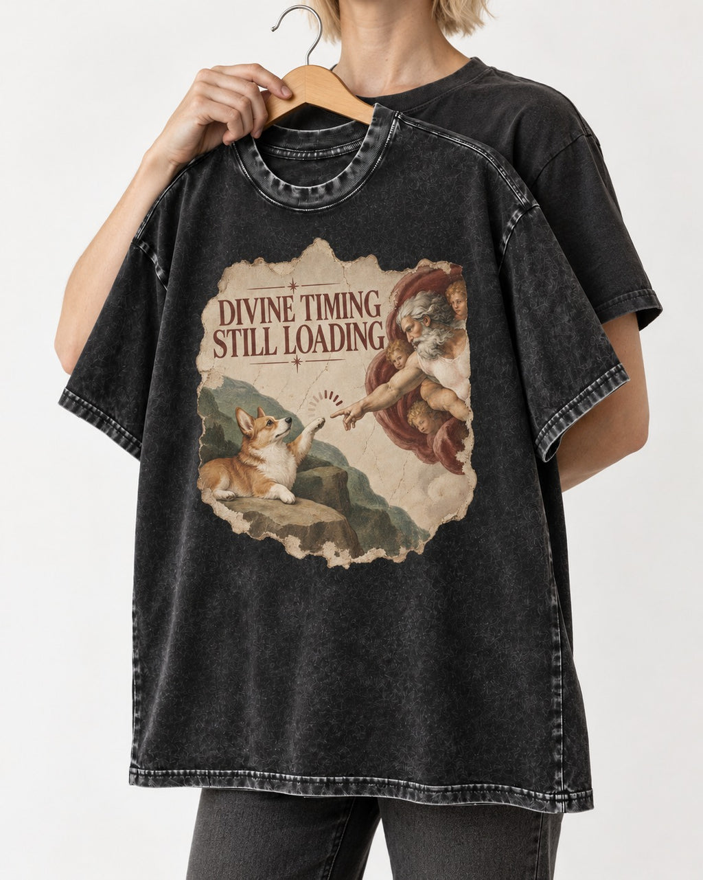 Corgi Divine Timing Still Loading Creation Parody Washed Tee in Black, held up on a hanger