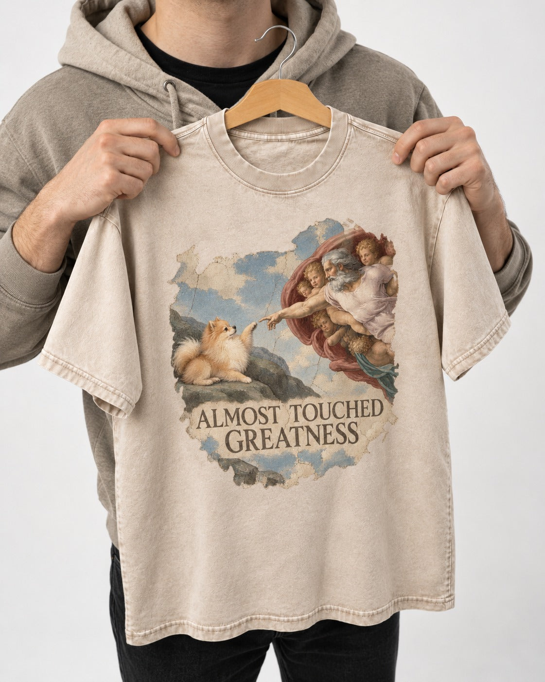 Pomeranian Almost Touched Greatness Fresco Graphic Washed Tee in Apricot, held up on a hanger